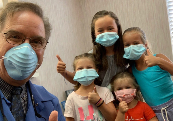 Dr. with a gaggle of young patients all giving the thumbs up.